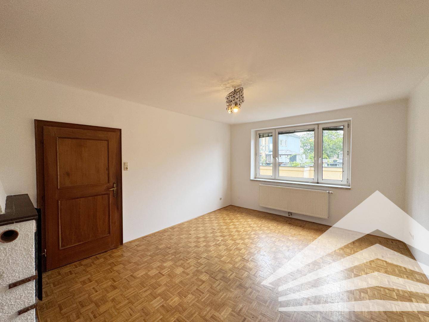 Heller Raum mit Parkettboden, einem Fenster mit Blick nach draußen und einem Heizkörper.