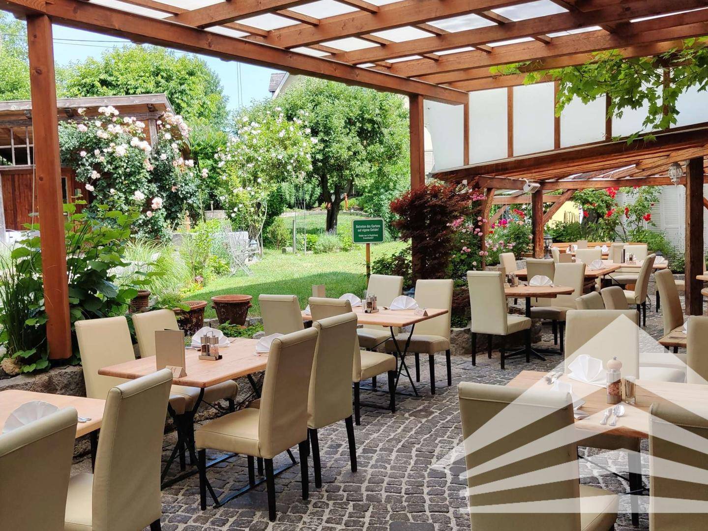 Weitläufige Terrasse mit vielen Tischen und Stühlen, umgeben von einem blühenden Garten.
