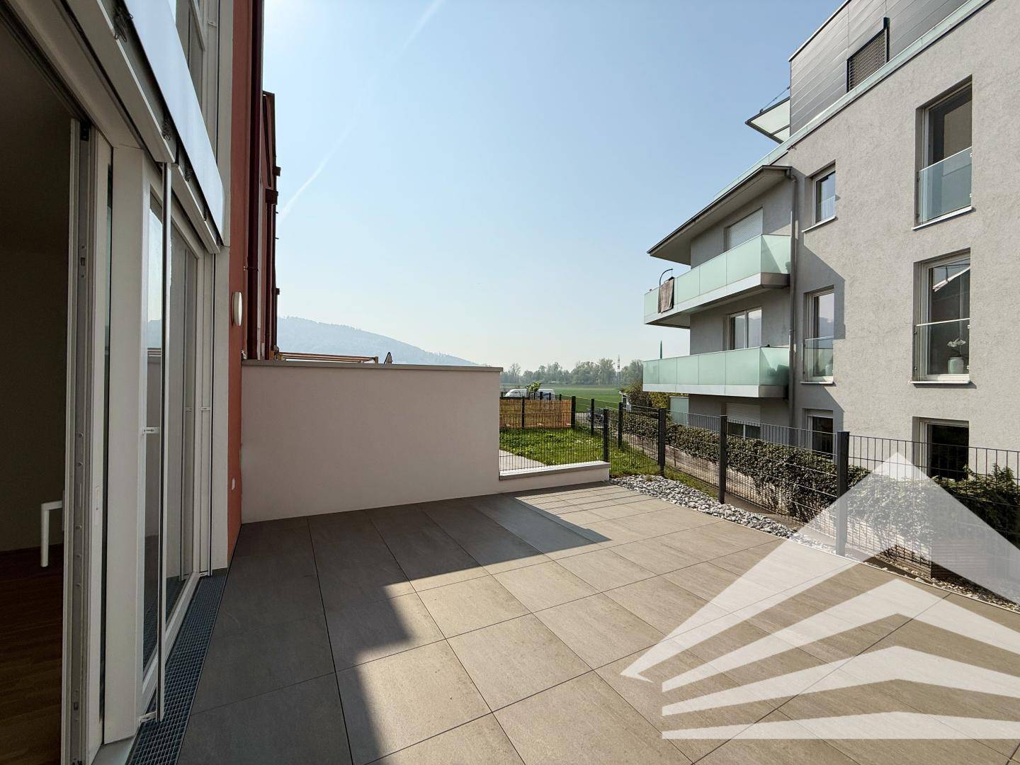 Helle Terrasse mit Fliesenboden und weitem Blick auf die grüne Umgebung und Berge.