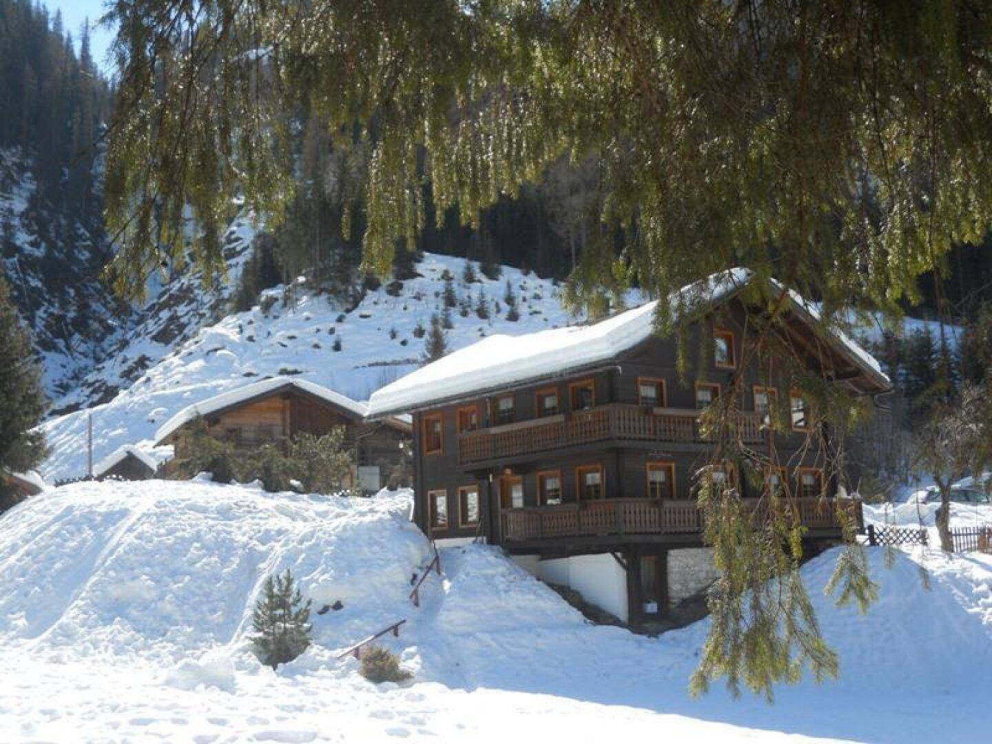 Traditionelles Holzchalet im Schnee mit Balkonen und Bergblick, umgeben von verschneiten Hängen.