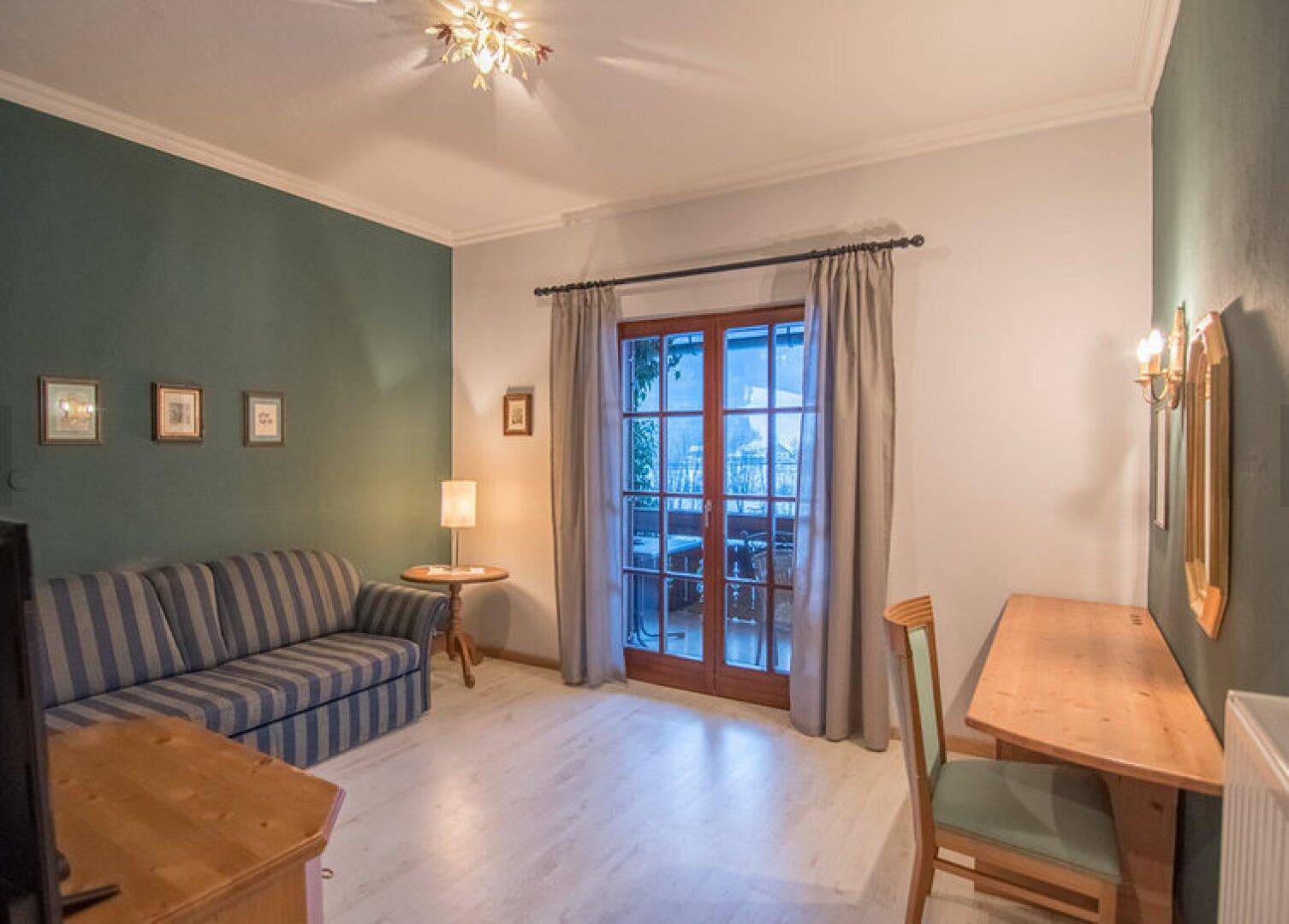 Wohnzimmer mit gestreiftem Sofa, Holzboden und Zugang zu einem Balkon oder einer Terrasse.