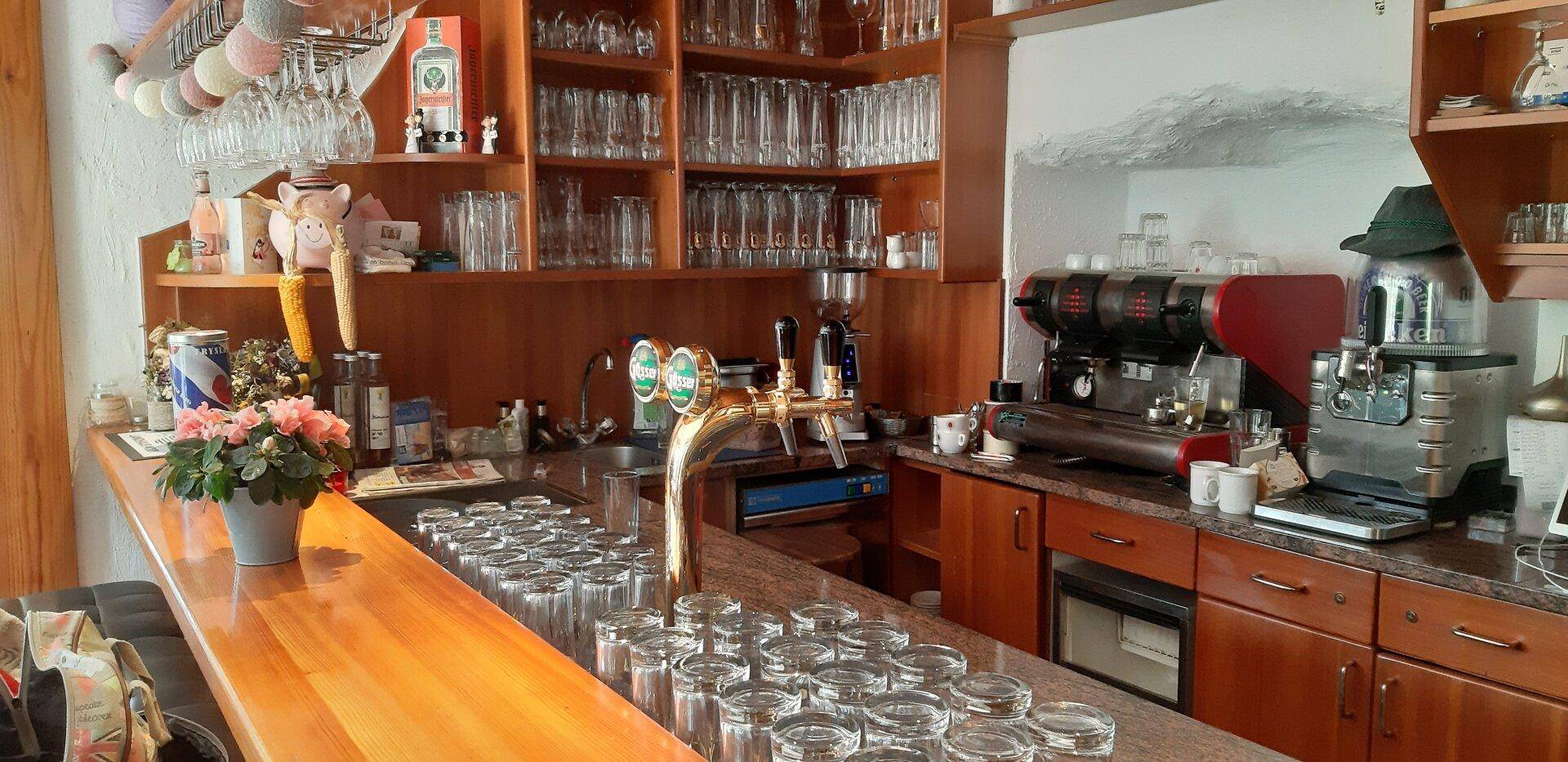 Gut ausgestattete Bar mit Holzarbeitsplatte, zahlreichen Gläsern und einer professionellen Kaffeemaschine.