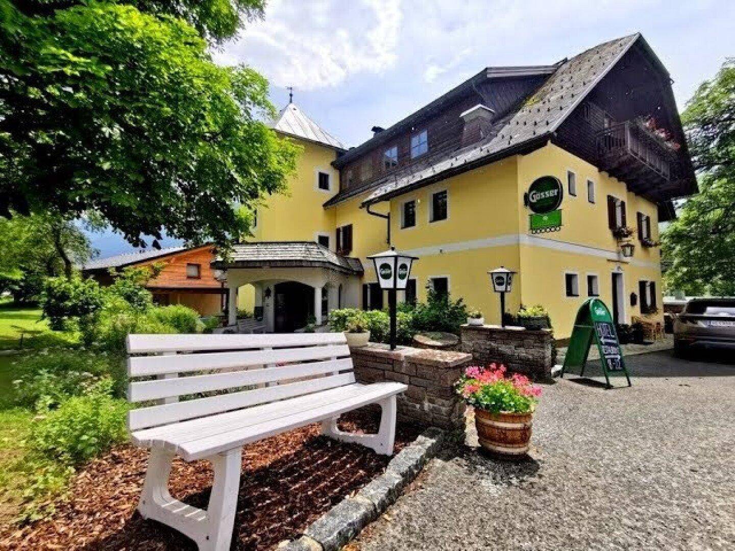 Historisches Gebäude mit gelber Fassade, traditioneller Architektur und einem weißen Gartenbank im Vordergrund.