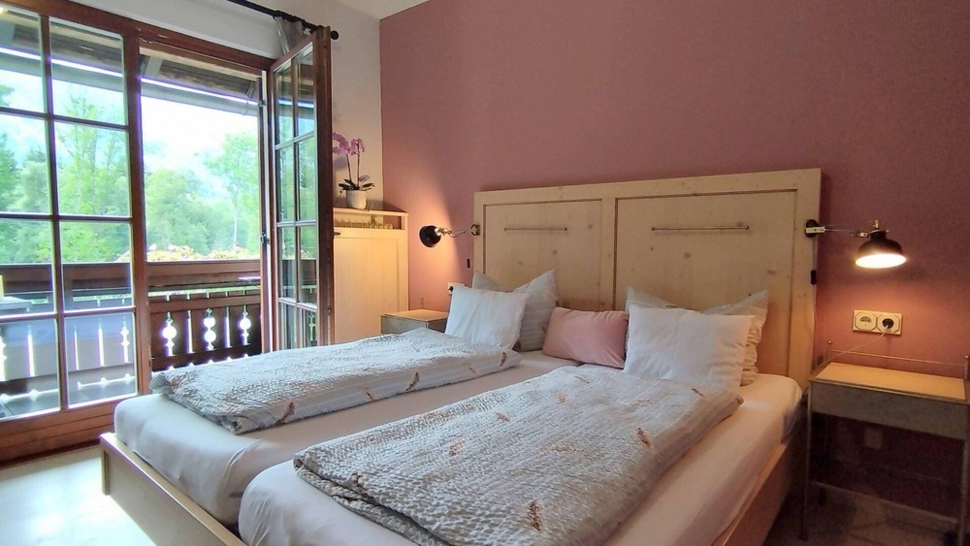 Gemütliches Schlafzimmer mit zwei Einzelbetten, rosa Wand und Zugang zu einem Balkon mit Bergblick.