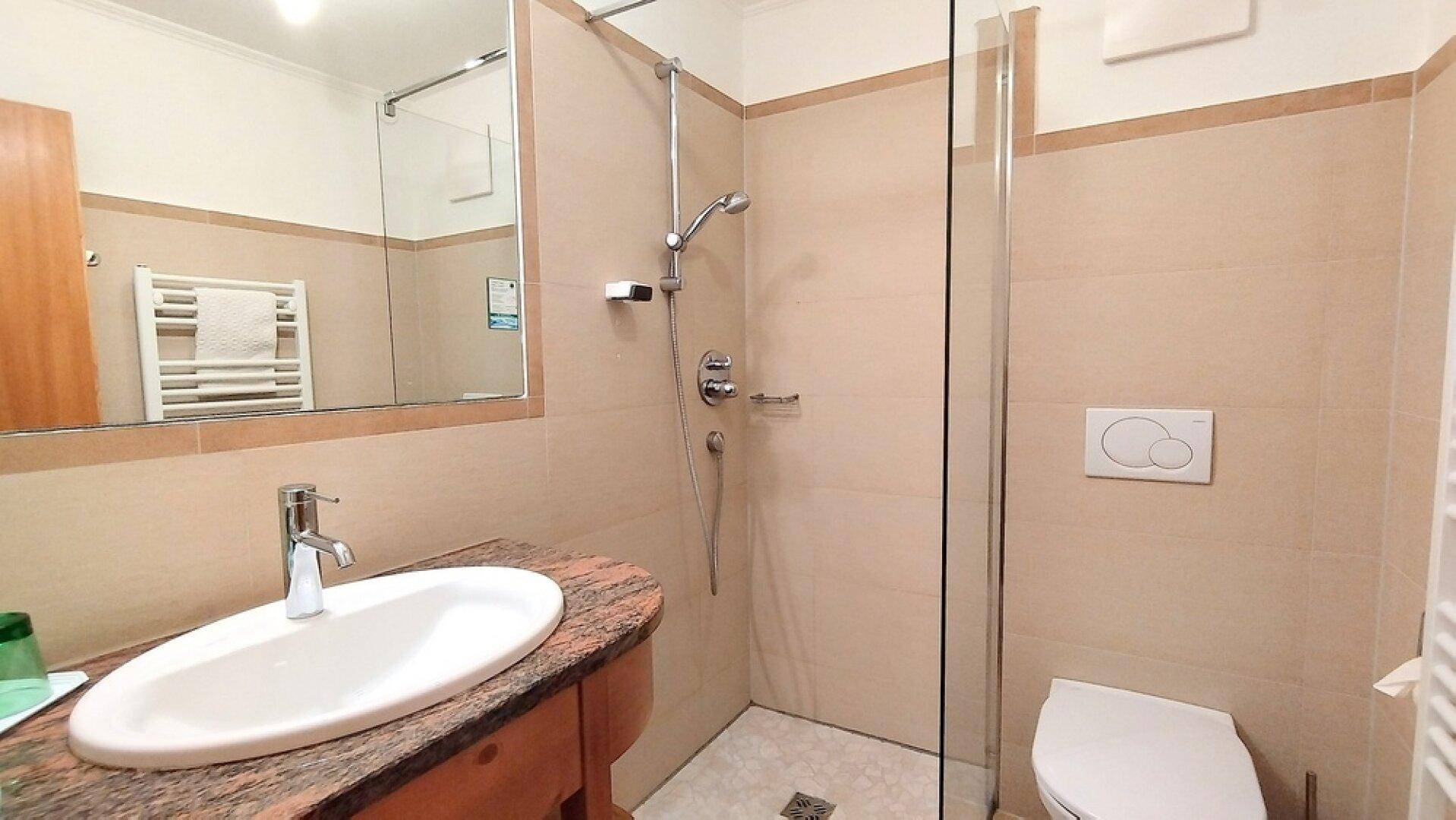 Helles Badezimmer mit Dusche, WC und Waschtisch, ausgestattet mit beigefarbenen Fliesen.