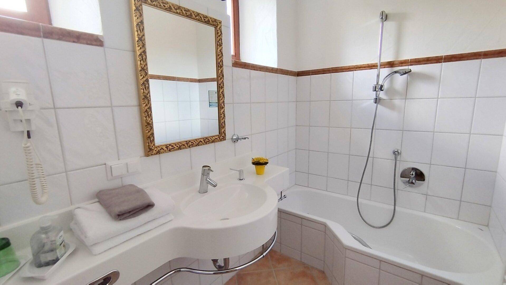 Klassisches Badezimmer mit Badewanne, Waschtisch und einem goldenen Spiegel, gefliest in Weiß.