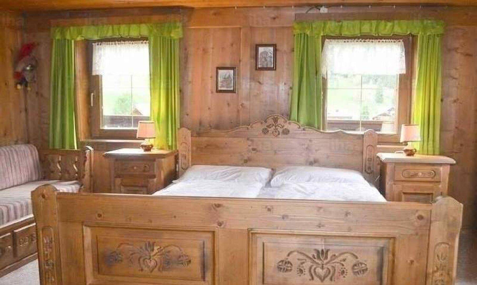 Gemütliches Schlafzimmer im alpinen Stil mit geschnitztem Holzdoppelbett und grünen Vorhängen.