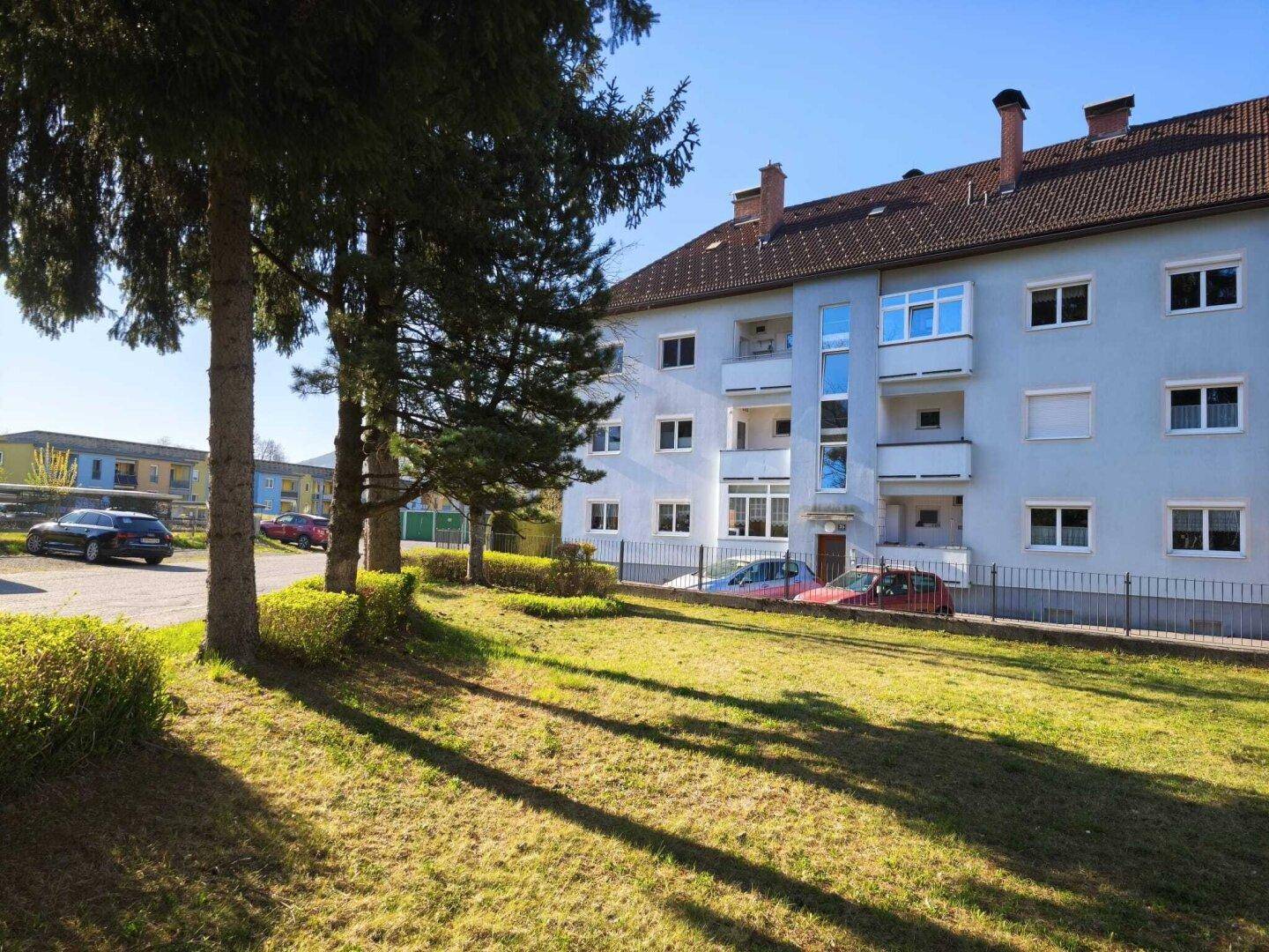 Mehrfamilienhaus mit gepflegter Grünfläche und Balkonen unter blauem Himmel.