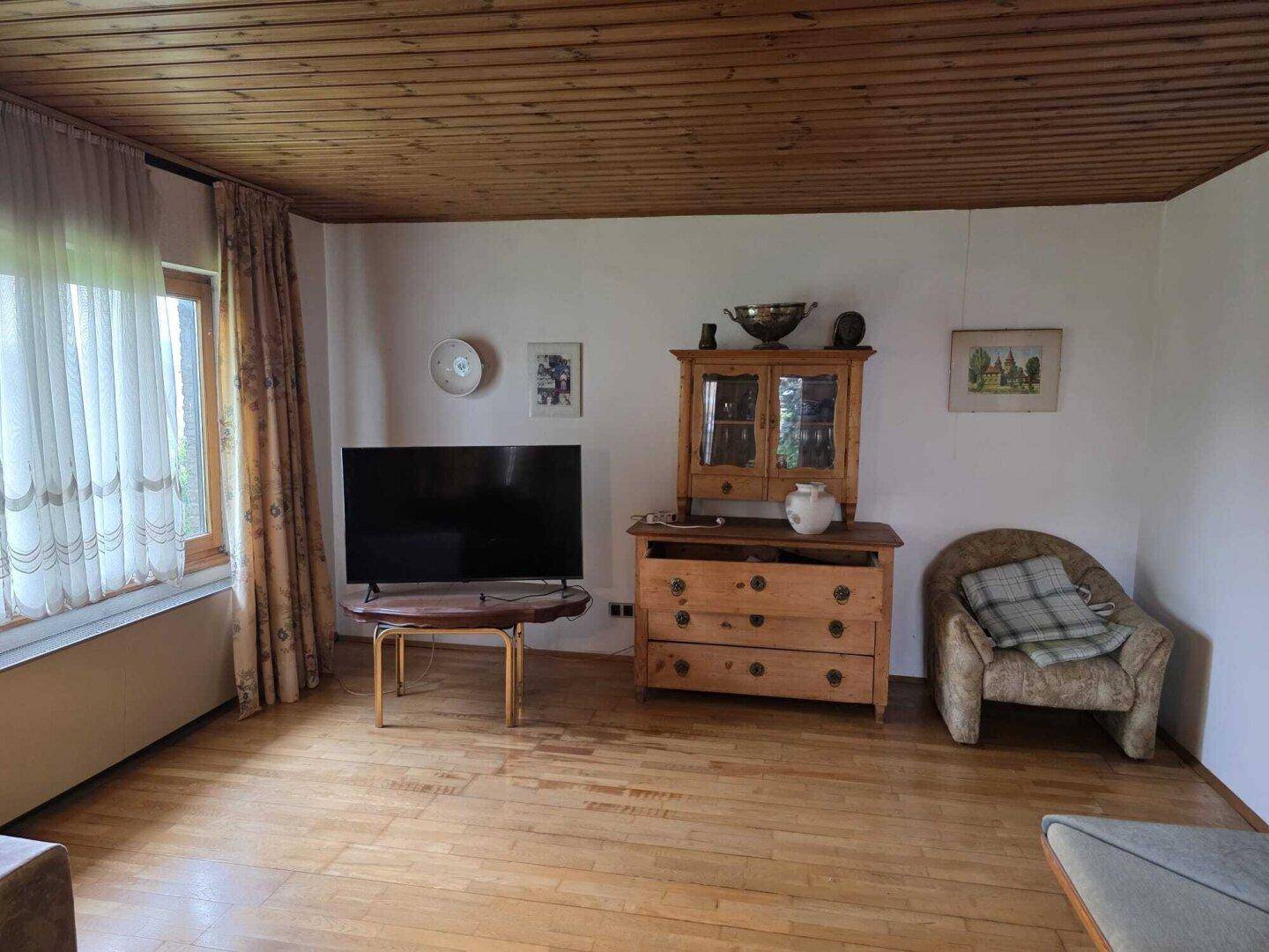Helles Wohnzimmer mit Holzdecke, Parkettboden, Fernseher und rustikalen Möbeln.