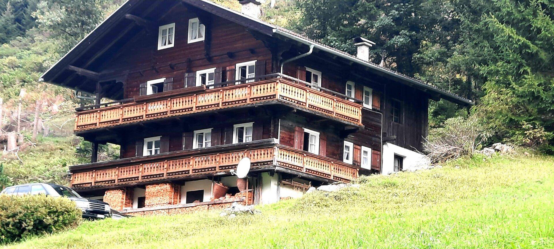 Charmantes Holzhaus im alpinen Stil, eingebettet in eine grüne Hanglage mit bewaldeten Bergen.
