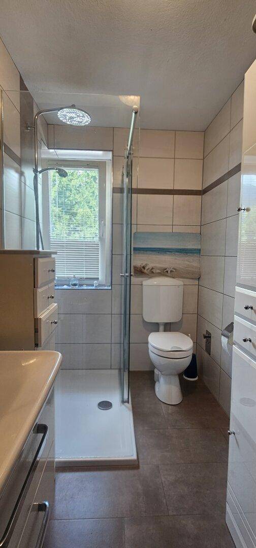 Modernes Badezimmer mit Duschkabine, WC und Fenster für natürliche Belüftung.