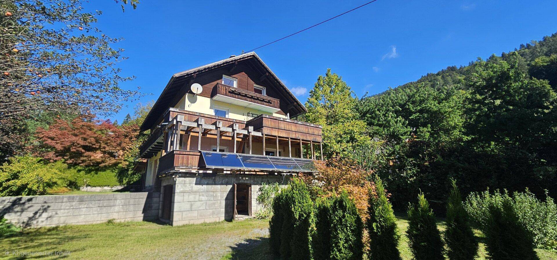 Traditionelles Haus mit Satteldach, Balkonen und Solarpaneelen, umgeben von viel Grün und Bergen.