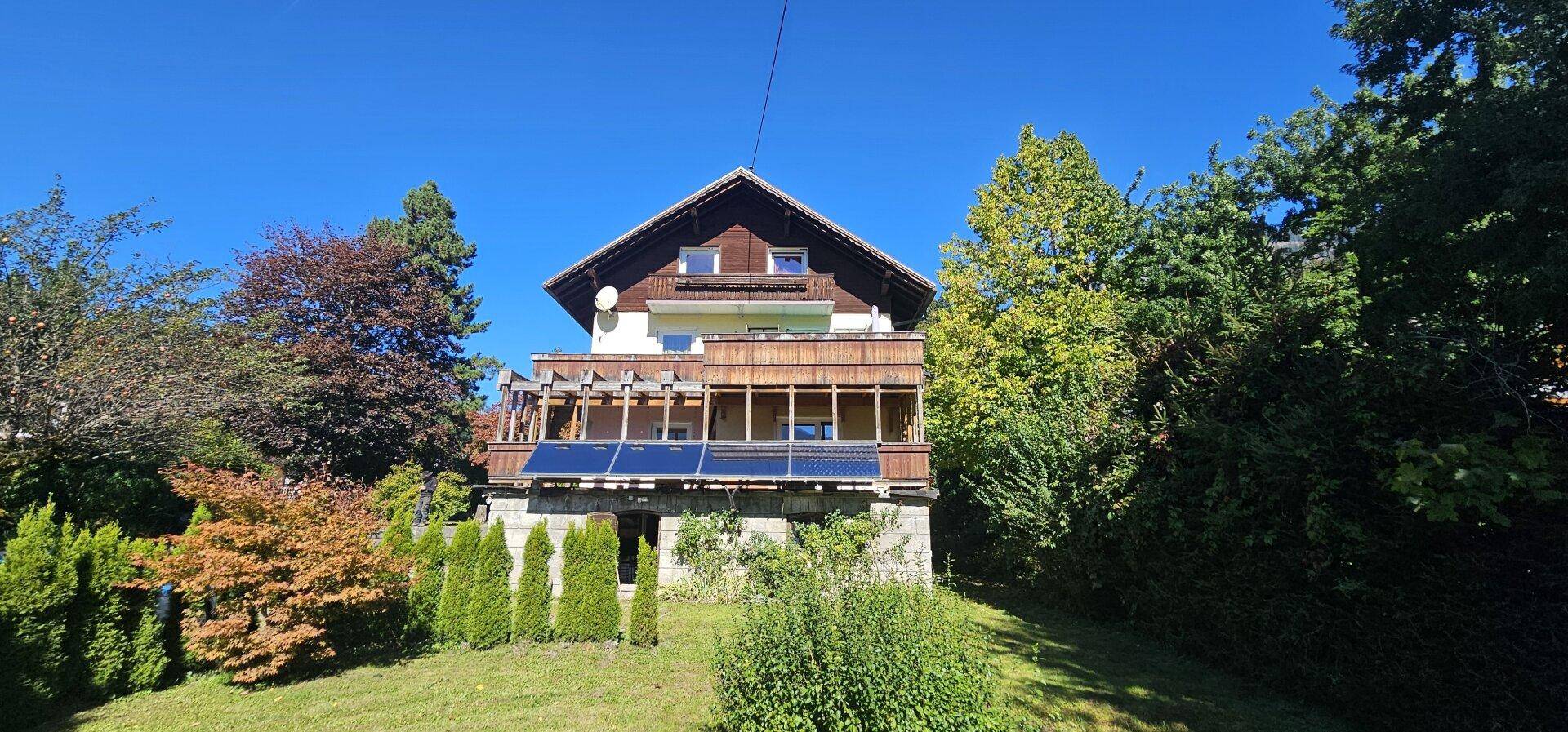 Freistehendes Haus mit mehreren Balkonen und Solaranlage, eingebettet in eine grüne Hügellandschaft.