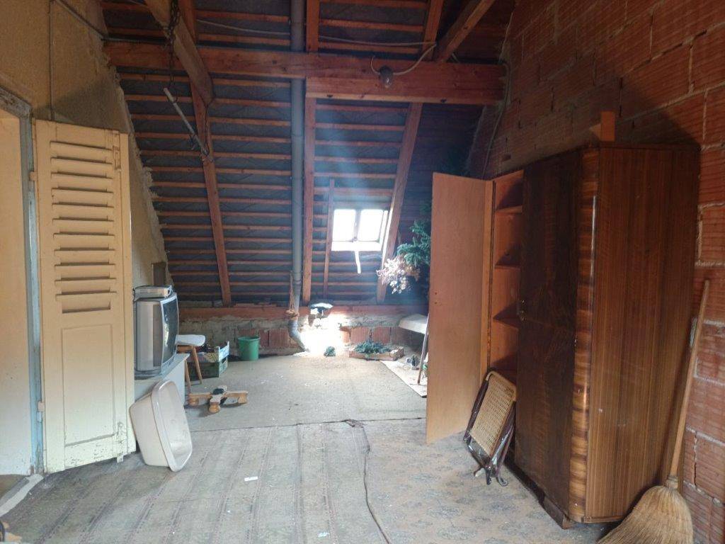Geräumiger Dachboden mit Holzbalken, Ziegelwänden und einem kleinen Fenster.