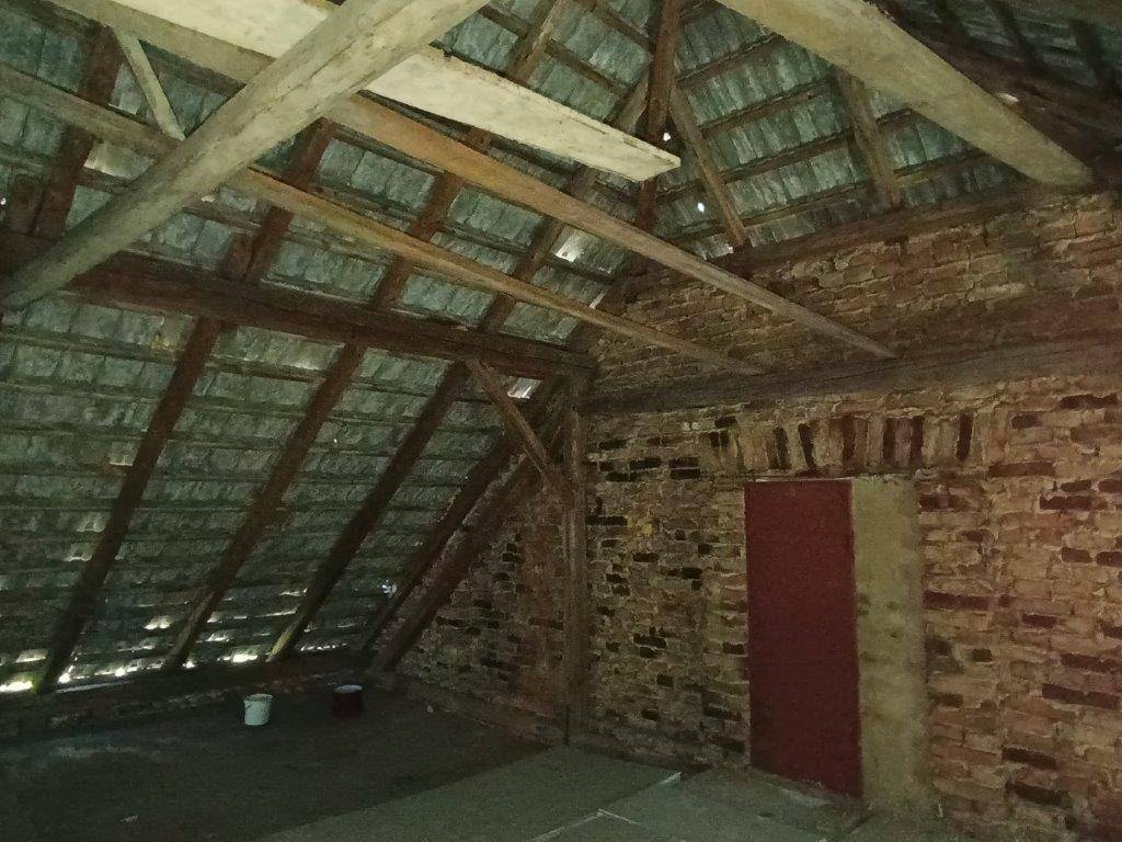 Dachboden mit freiliegenden Ziegelwänden, Holzbalken und einer kleinen roten Tür, die einen rustikalen Charme verleiht.