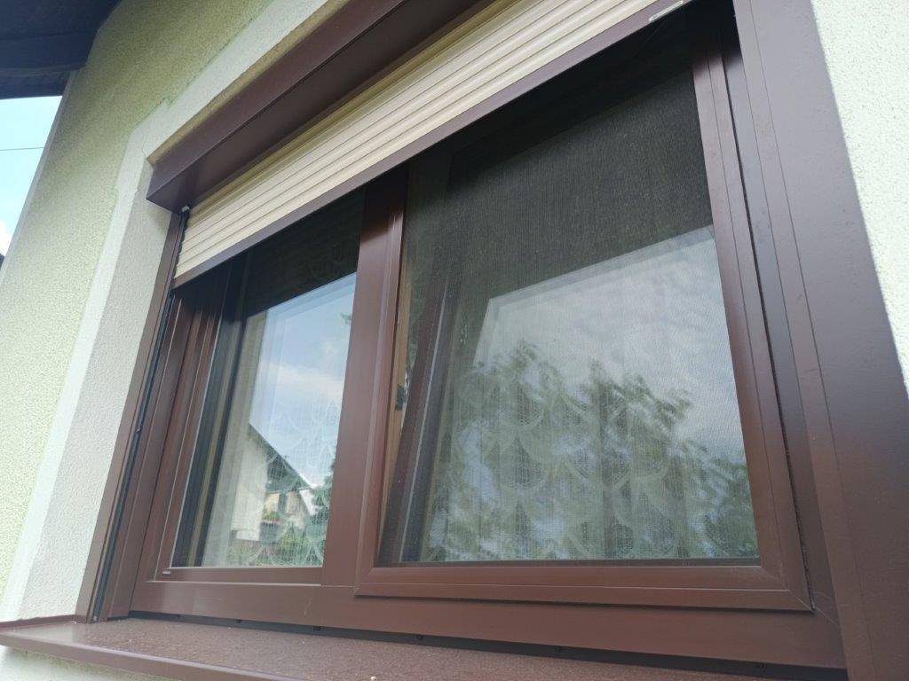 Nahaufnahme eines Fensters mit braunem Rahmen und Rollladen an der hellen Hausfassade.