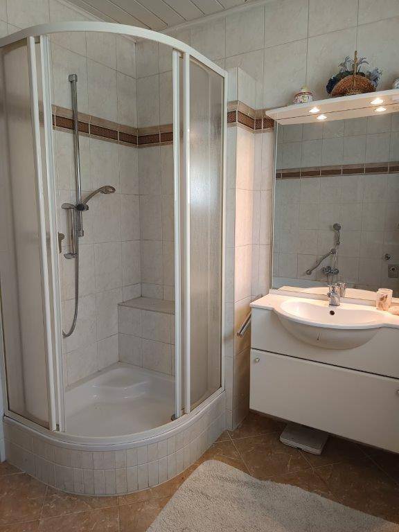 Badezimmer mit Duschkabine, Waschbecken und Spiegel, gefliest in warmen Beigetönen.