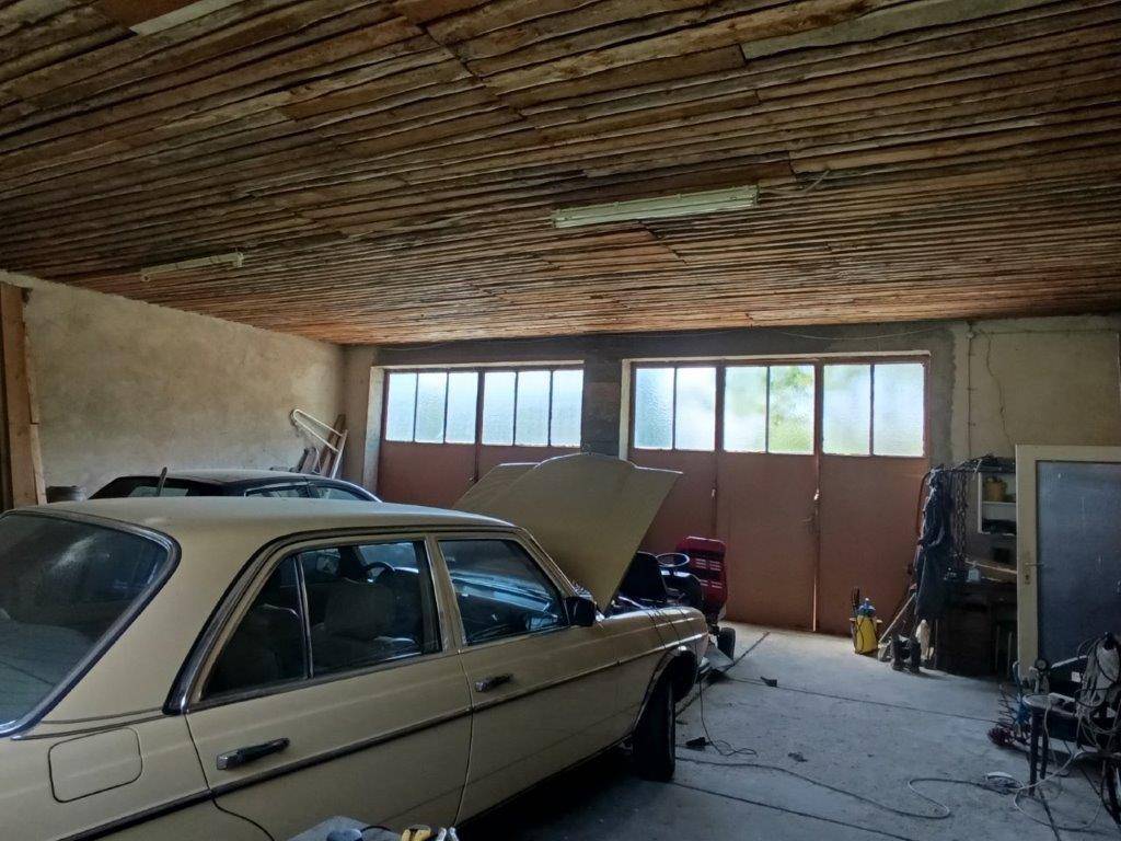 Innenansicht einer Garage mit Blick auf die Tore und einen älteren Mercedes unter einer Holzplankendecke.