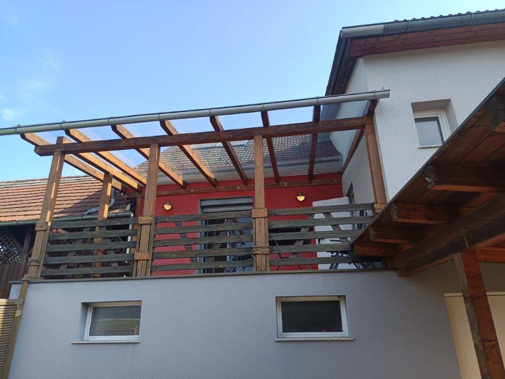Überdachte Terrasse mit Holzkonstruktion und roter Wand, bietet Schutz und Ausblick.