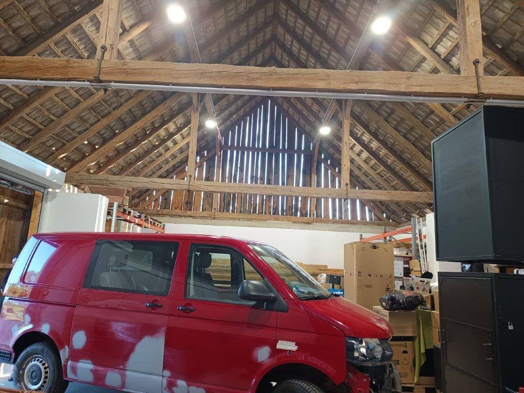 Geräumige Garage mit einem roten Lieferwagen, einem alten Traktor und sichtbarem Holzdachstuhl.