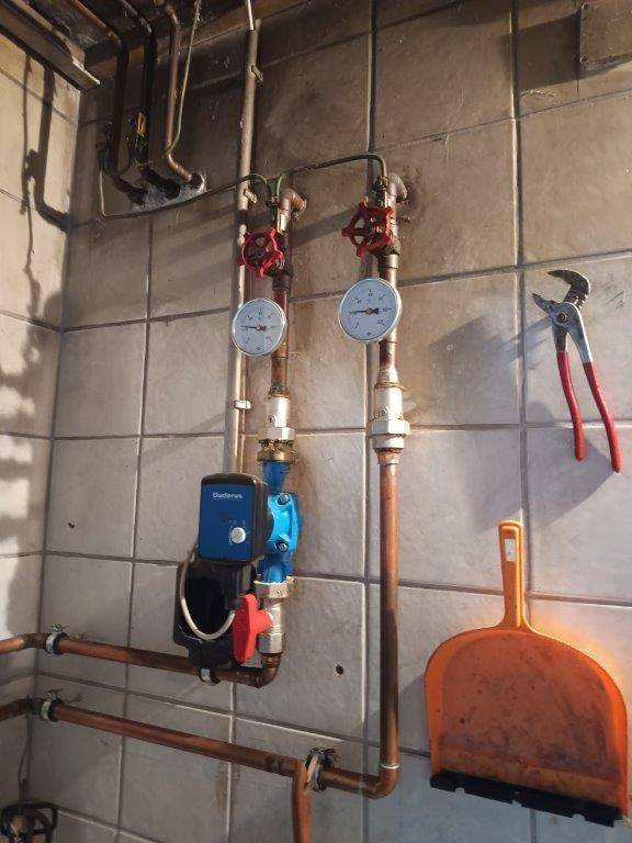 Heizungsinstallation mit Kupferrohren, Manometern und einer Umwälzpumpe.