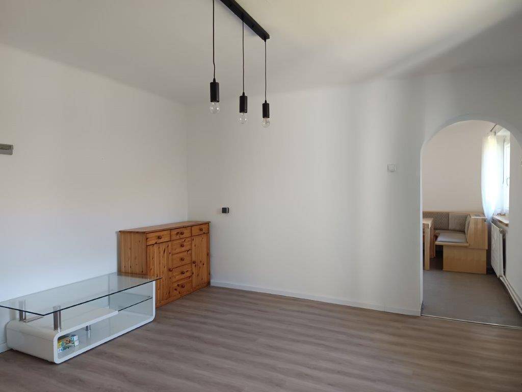 Geräumiges Wohnzimmer mit Laminatboden, weiß gestrichenen Wänden und Holzkredenz.