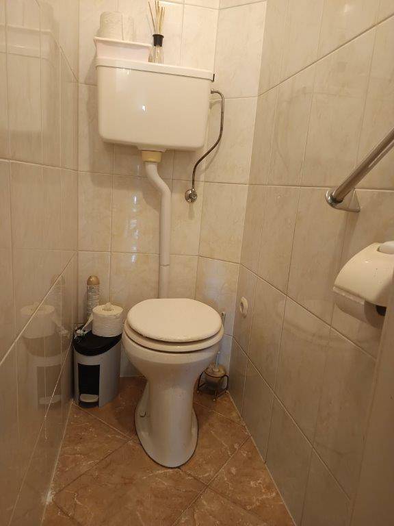 Kleines WC mit Toilette und beigefarbenen Fliesen an den Wänden, funktional und sauber.
