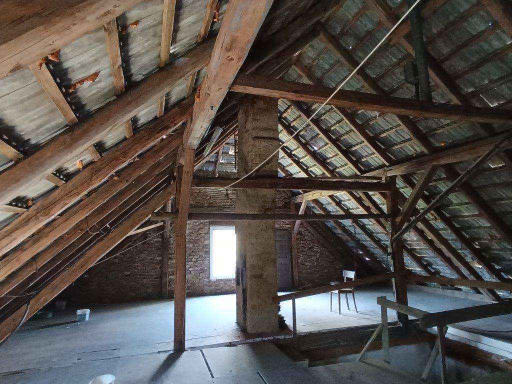 Geräumiger, unfertiger Dachboden mit sichtbaren Holzbalken, einem Fenster und einer Bodenöffnung.