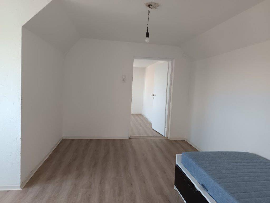 Schlafzimmer mit Laminatboden, weißen Wänden und einem Bett, bereit zur Einrichtung.
