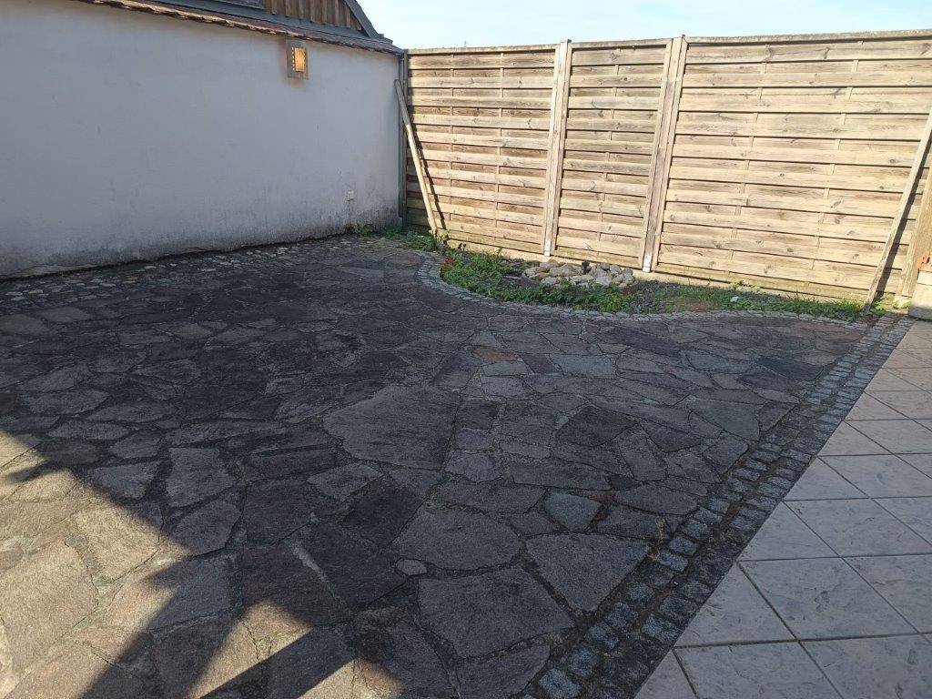 Gepflasterter Terrassenbereich mit Natursteinplatten und Holzzaun, ideal für Entspannung.