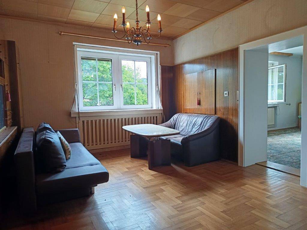 Gemütliches Wohnzimmer mit Fischgrätparkett, Holzdecke und einem Fenster mit Blick ins Grüne.