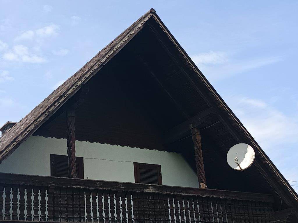 Detailansicht des traditionellen Holzbalkons und des Satteldachs mit Satellitenschüssel.