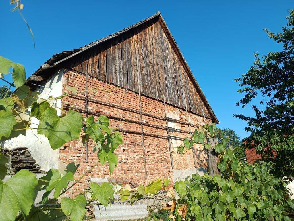 Detailansicht der alten Scheunenwand mit sichtbarem Ziegelmauerwerk und Holzbalken unter blauem Himmel.