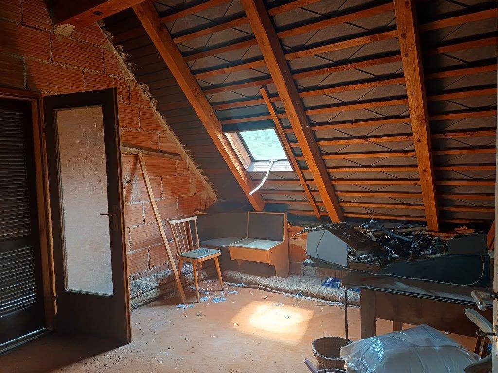 Unausgebauter Dachboden mit sichtbaren Holzbalken, Ziegelwänden und Dachfenster.
