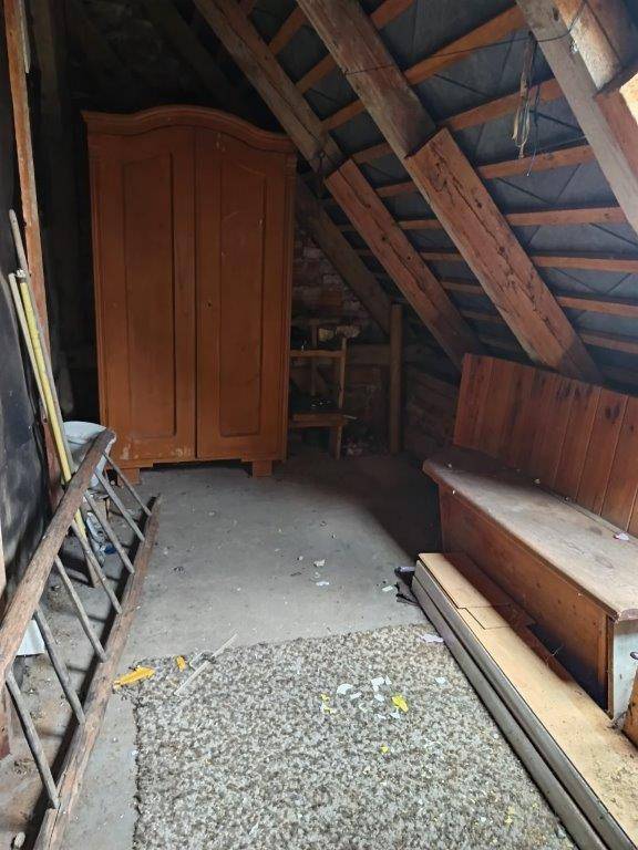 Dachbodenbereich mit Holzbalken, einem alten Schrank und einer Leiter.