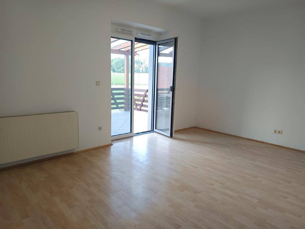 Geräumiges Wohnzimmer mit hellem Laminatboden und Zugang zu einer überdachten Terrasse.