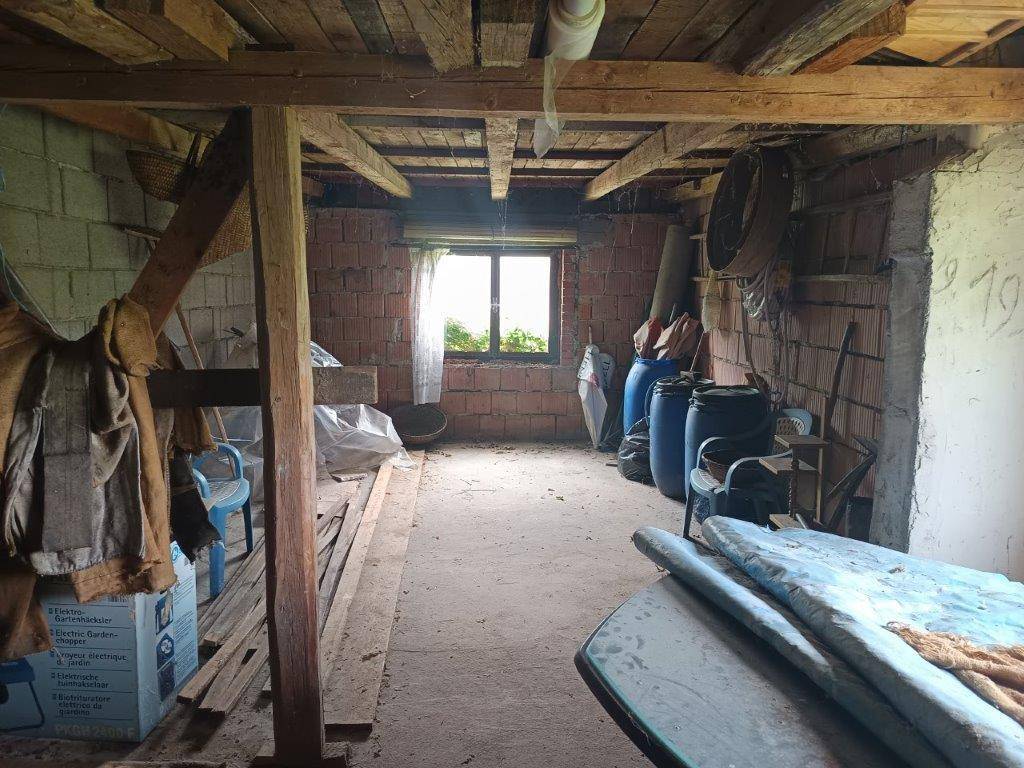 Unausgebauter Raum mit sichtbaren Holzbalken, Ziegelwänden und einem Fenster.
