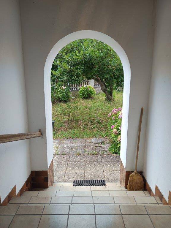 Eingangsbereich mit gefliestem Boden, weißem Rundbogen und Blick in den Garten.