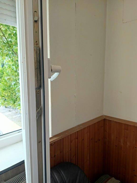 Detailaufnahme eines geöffneten Fensters mit weißem Rahmen und Holztäfelung an der Wand.