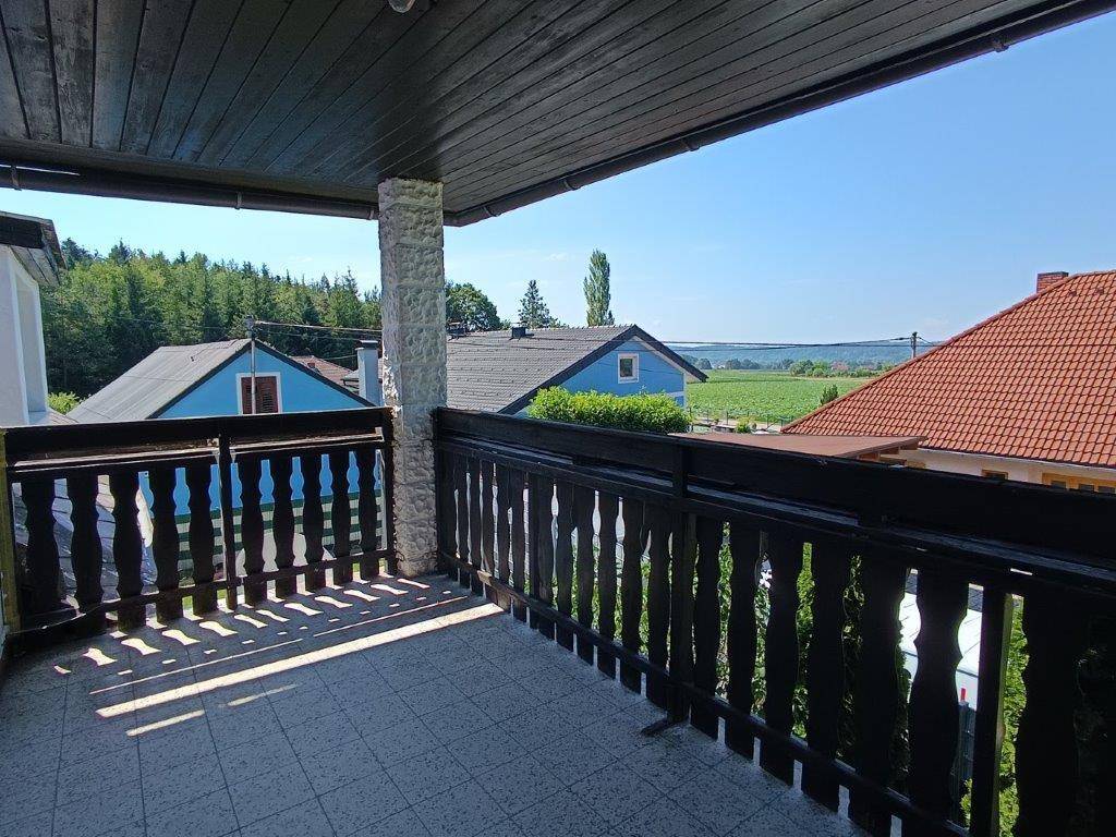 Sonniger Balkon mit traditionellem Holzgeländer und Fliesenboden, mit Blick auf die Landschaft.
