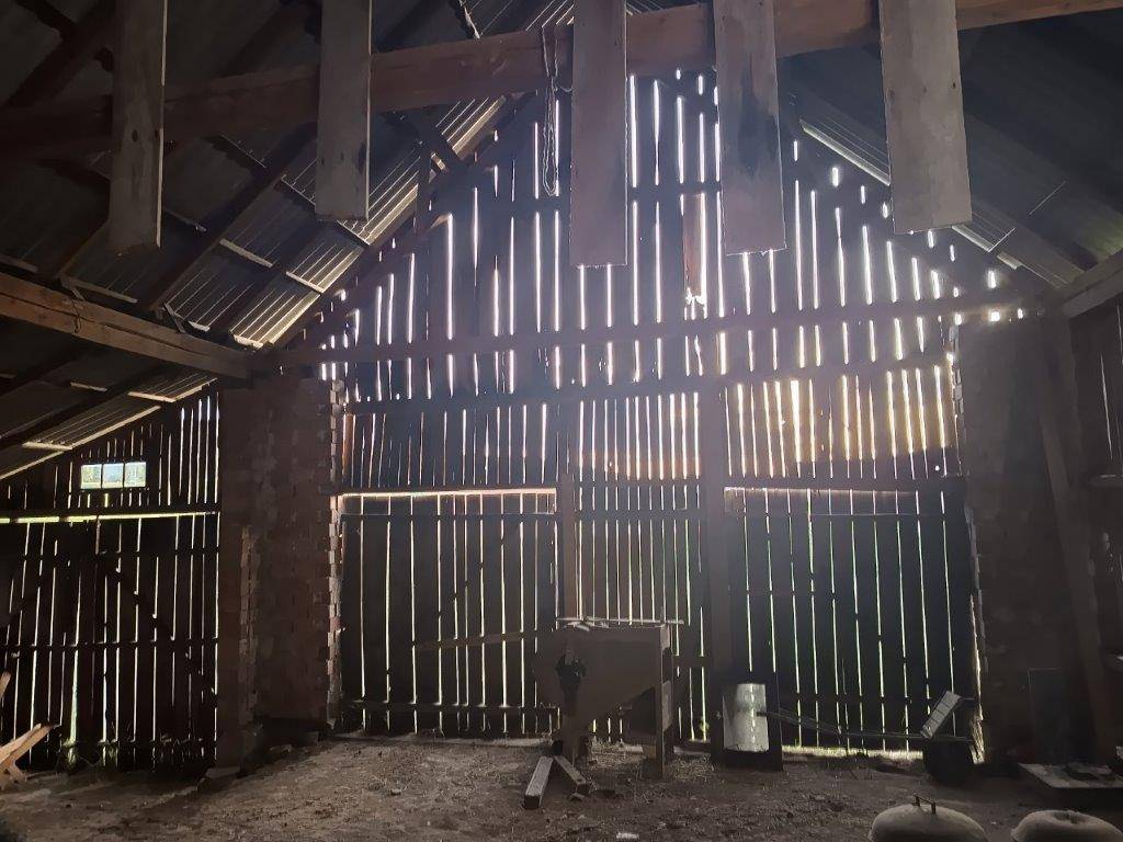 Dachboden oder Scheuneninnenraum mit sichtbaren Holzbalken und Dachkonstruktion, durch die Licht einfällt.