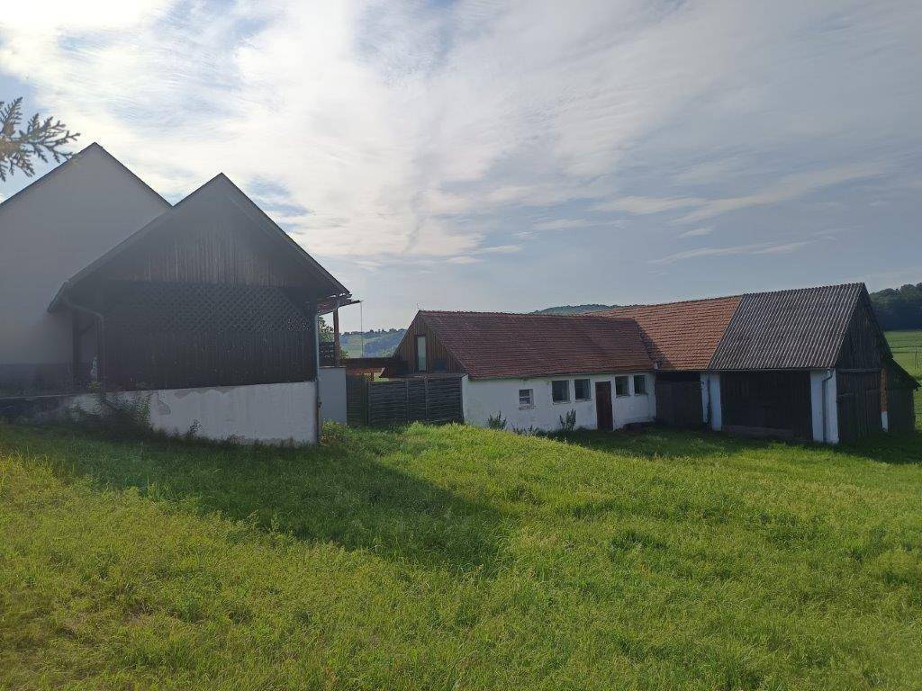 Ländliche Gebäude mit traditionellen Dächern, umgeben von weiten grünen Feldern.