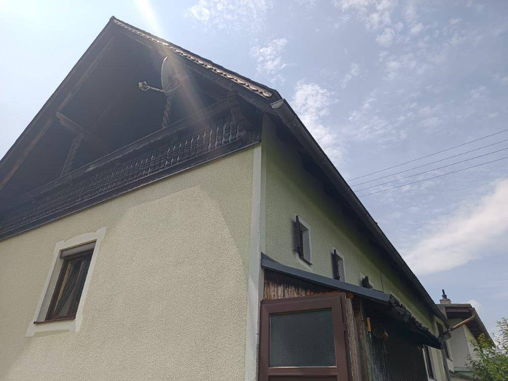 Nahaufnahme der Hausfassade mit Holzbalkon, Satteldach und Dachfenstern unter blauem Himmel.