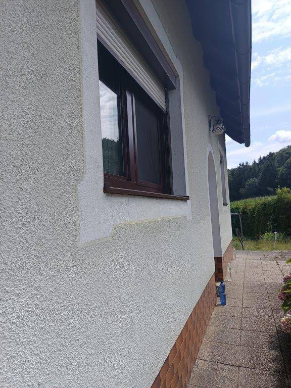 Seitenansicht der Hausfassade mit Fenster, Rollladen und gepflastertem Zugangsbereich.