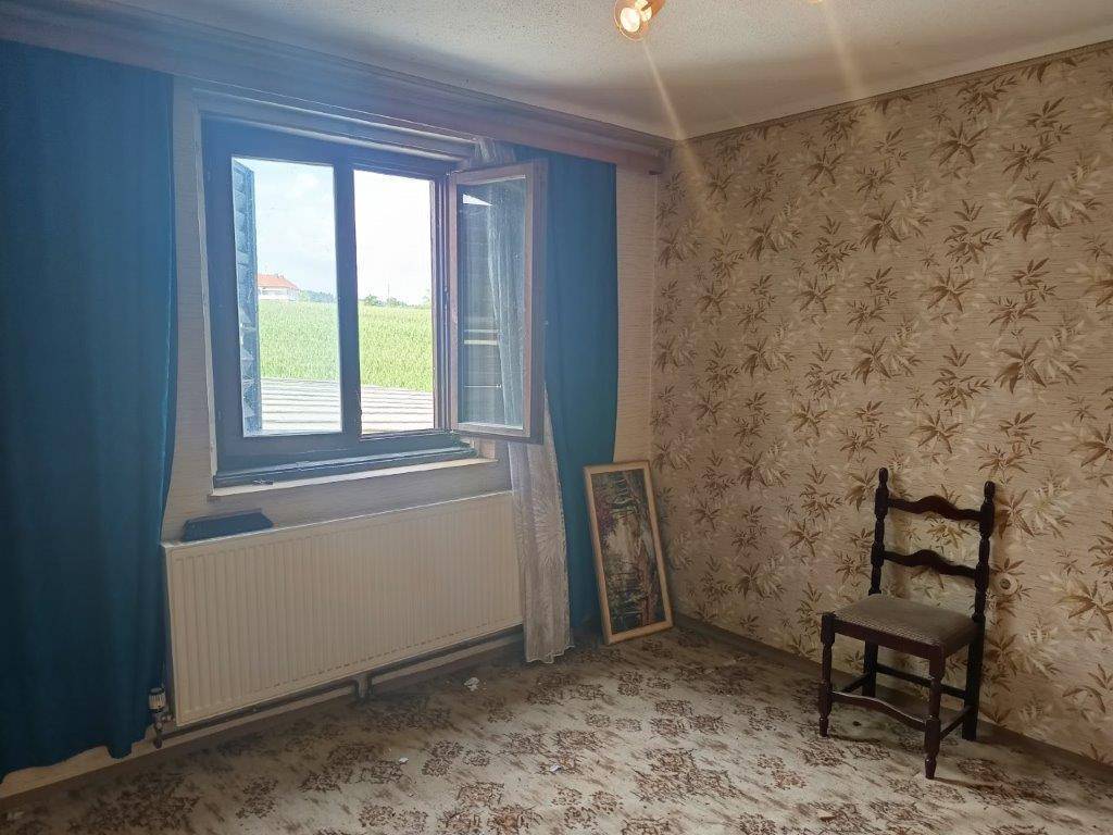 Zimmer mit gemusterter Tapete, Teppichboden und Blick auf ein Feld.