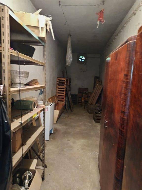 Langer, schmaler Lagerraum im Keller mit Regalen und alten Möbeln, ausgestattet mit einem Abluftventilator.