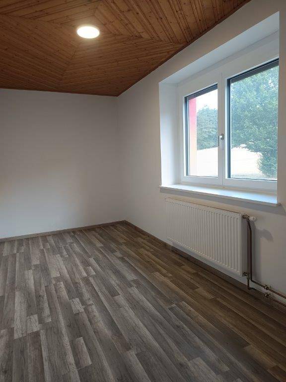 Helles Zimmer mit Laminatboden, Holzdecke und Fenster, ausgestattet mit einem Heizkörper.