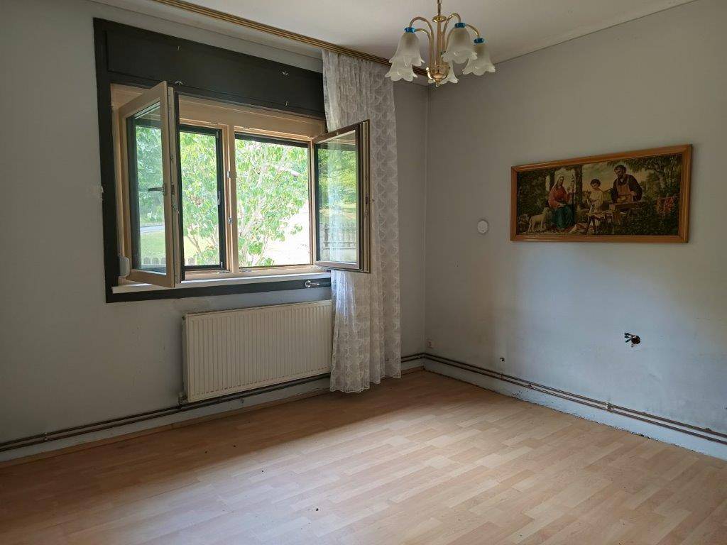 Helles Zimmer mit Laminatboden, Fensterblick ins Grüne und einem klassischen Kronleuchter.