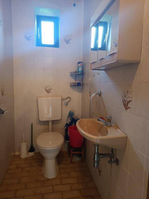 Kleines WC mit Fliesen, Waschbecken und Fenster, in einem älteren Stil.
