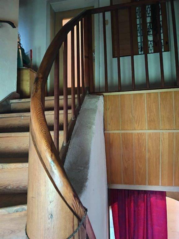 Geschwungene Holztreppe mit Geländer in einem Flurbereich mit Holzelementen.